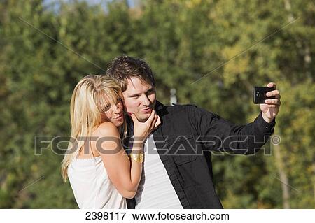 Young couple taking a self-portrait with their camera in a park; Edmonton, Alberta, Canada View Large Photo Image Stock Photo - Young couple taking a self-portrait with their camera in a park; Edmonton, Alberta, Canada. Fotosearch