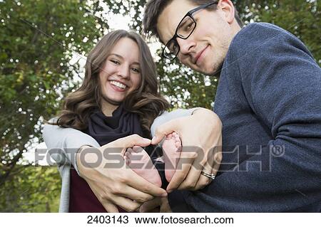 Stock Image - Young couple with a baby making a heart shape on the baby's feet; Edmonton, Alberta, Canada. Fotosearch