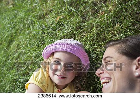 Picture - Young girl laying on the grass with her mother laughing; Toronto, Ontario, Canada. Fotosearch