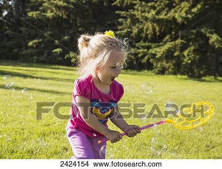 Picture - Young girl running in a park making bubbles; St. Albert, Alberta, Canada. Fotosearch