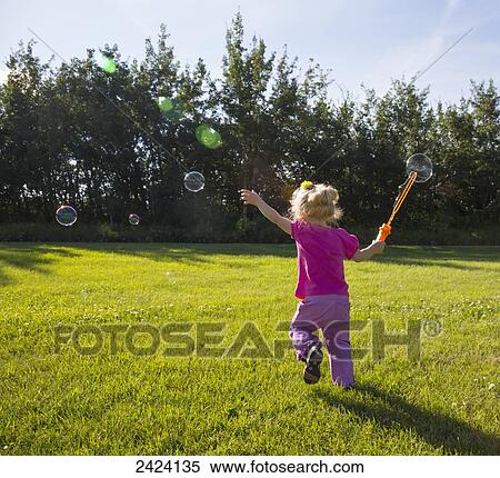 Stock Photography - Young girl running in a park making bubbles; St. Albert, Alberta, Canada. Fotosearch