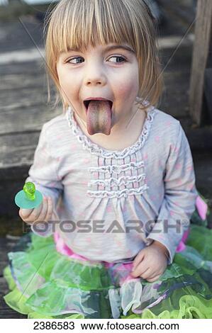 Stock Image - Young girl sticking out tongue after sucking on green ring candy; Toronto, Ontario, Canada. Fotosearch