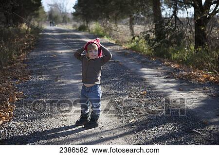 Stock Image - Young girl stops on a country road with hands on her head in pixie hat and winter boots; Ontario, Canada. Fotosearch