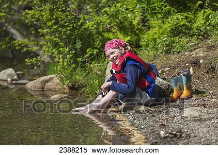 Young girl wearing a lifejacket and sitting on a sun drenched shore of Byers Lake soaking her bare feet in the water, Byers lake campground, Denali State Park; Alaska, United States of America View Large Photo Image Stock Photography - Young girl wearing a lifejacket and sitting on a sun drenched shore of Byers Lake soaking her bare feet in the water, Byers lake campground, Denali State Park; Alaska, United States of America. Fotosearch