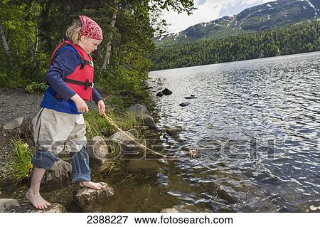 Young girl with bare feet wearing a red bandana and lifejacket playing with a homemade toy wood raft on a string at Byers Lake, Denali State Park; Alaska, United States of America View Large Photo Image Stock Photo - Young girl with bare feet wearing a red bandana and lifejacket playing with a homemade toy wood raft on a string at Byers Lake, Denali State Park; Alaska, United States of America. Fotosearch
