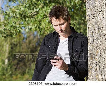 Young man texting in a park; Edmonton, Alberta, Canada View Large Photo Image Stock Photograph - Young man texting in a park; Edmonton, Alberta, Canada. Fotosearch