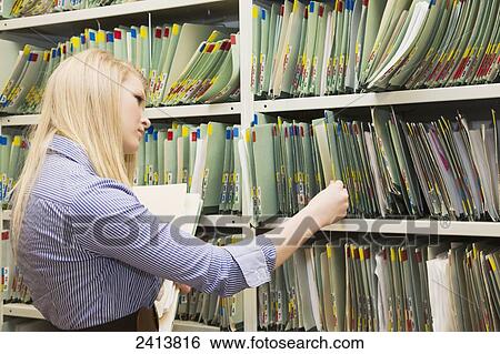 Stock Photograph - Young woman filing documents at an accounting office; Edmonton, Alberta, Canada. Fotosearch