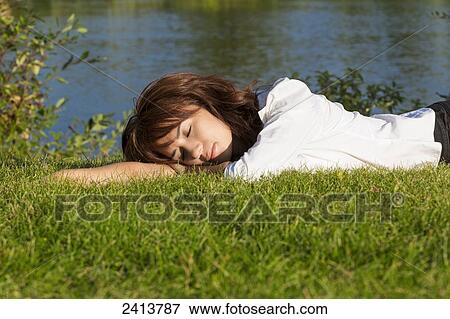 Stock Photo - Young woman laying down and relaxing in a park; Edmonton, Alberta, Canada. Fotosearch