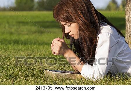 Stock Photography - Young woman praying with her Bible in a park; Edmonton, Alberta, Canada. Fotosearch