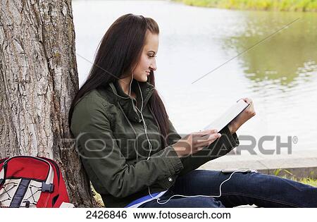 Young woman reading from a tablet outdoors in a park; St. Albert, Alberta, Canada View Large Photo Image Stock Photograph - Young woman reading from a tablet outdoors in a park; St. Albert, Alberta, Canada. Fotosearch