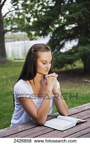 Young woman reading her Bible and praying outdoors in a park; St. Albert, Alberta, Canada View Large Photo Image Stock Photo - Young woman reading her Bible and praying outdoors in a park; St. Albert, Alberta, Canada. Fotosearch
