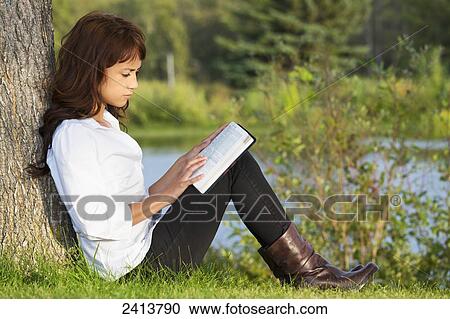 Stock Image - Young woman reading her Bible in a park; Edmonton, Alberta, Canada. Fotosearch
