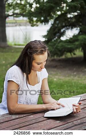 Stock Photograph - Young woman reading her Bible outdoors in a park; St. Albert, Alberta, Canada. Fotosearch