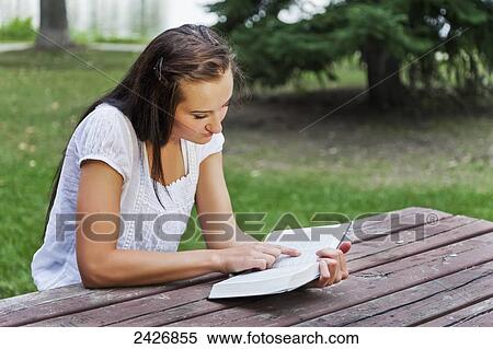 Stock Photography - Young woman reading her Bible outdoors in a park; St. Albert, Alberta, Canada. Fotosearch