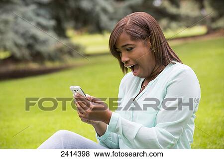 Young woman reads something shocking on her smart phone in a park; Edmonton, Alberta, Canada View Large Photo Image Stock Photo - Young woman reads something shocking on her smart phone in a park; Edmonton, Alberta, Canada. Fotosearch