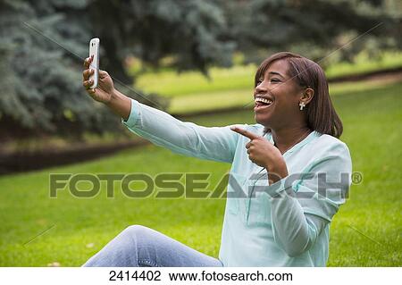 Young woman taking a self-portrait with her smart phone in the park; Edmonton, Alberta, Canada View Large Photo Image Stock Image - Young woman taking a self-portrait with her smart phone in the park; Edmonton, Alberta, Canada. Fotosearch