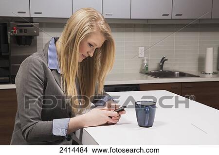 Young woman texting on her break in the lunch room at the office; Edmonton, Alberta, Canada View Large Photo Image Stock Photo - Young woman texting on her break in the lunch room at the office; Edmonton, Alberta, Canada. Fotosearch - Search Stock Images, Mural Photographs, Pictures, and Clipart Photos