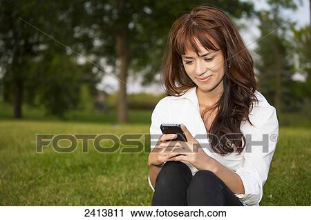 Young woman using a cell phone in a park; Edmonton, Alberta, Canada View Large Photo Image Stock Image - Young woman using a cell phone in a park; Edmonton, Alberta, Canada. Fotosearch