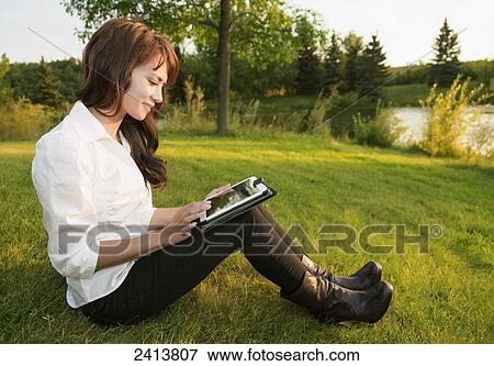 Young woman using her tablet in a park; Edmonton, Alberta, Canada View Large Photo Image Stock Photo - Young woman using her tablet in a park; Edmonton, Alberta, Canada. Fotosearch