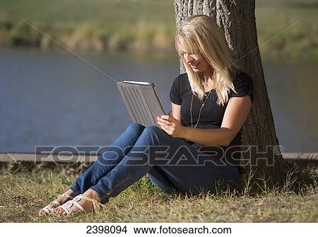 Picture - Young woman with a tablet in a park; Edmonton, Alberta, Canada. Fotosearch