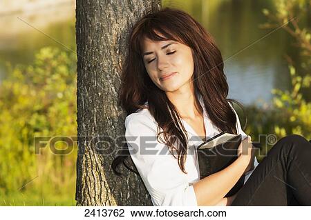 Stock Image - Young woman with her Bible in a park; Edmonton, Alberta, Canada. Fotosearch