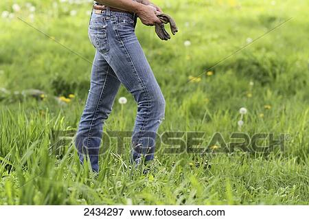 Stock Photo - A female walking in grass and wildflowers holding work gloves; Ellston, Iowa, United States of America. Fotosearch