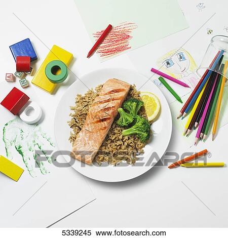 Stock Photography - A healthy meal of salmon, rice and broccoli sitting on a plate on top of kid's drawing supplies and artwork. Fotosearch
