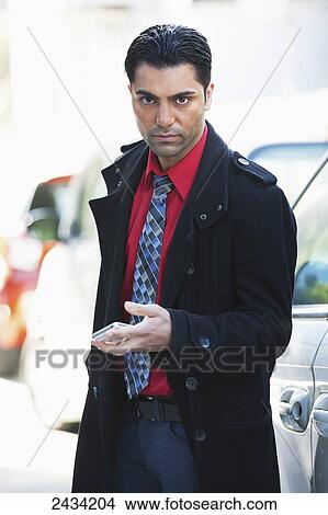 Picture - A man in a jacket and tie is standing by his car using his cell phone; San Francisco, California, United States of America. Fotosearch