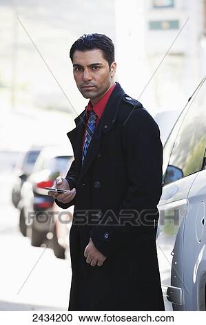 Stock Image - A man in a jacket and tie is standing by his car using his cell phone; San Francisco, California, United States of America. Fotosearch