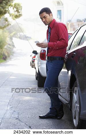 Stock Image - A man in a shirt and tie standing by his car using his cell phone; San Francisco, California, United States of America. Fotosearch