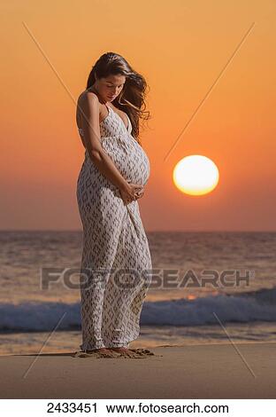 A pregnant woman stands on a beach at the water's edge at sunset with orange sky; Tarifa, Cadiz, Andalusia, Spain View Large Photo Image Stock Image - A pregnant woman stands on a beach at the water's edge at sunset with orange sky; Tarifa, Cadiz, Andalusia, Spain. Fotosearch
