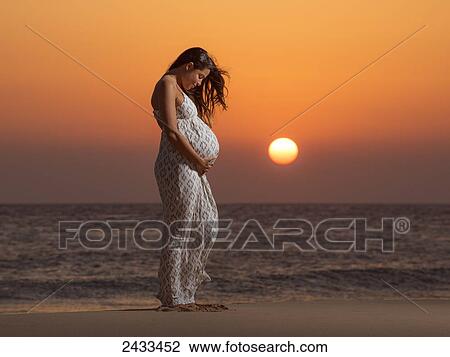 A pregnant woman stands on a beach at the water's edge at sunset with orange sky; Tarifa, Cadiz, Andalusia, Spain View Large Photo Image Stock Image - A pregnant woman stands on a beach at the water's edge at sunset with orange sky; Tarifa, Cadiz, Andalusia, Spain. Fotosearch