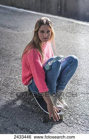 Stock Photograph - A teenage girl sitting on a skateboard; Tarifa, Cadiz, Andalusia, Spain. Fotosearch