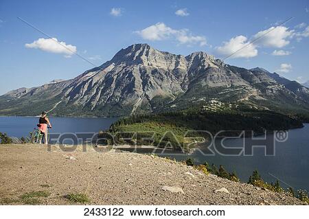 Stock Image - A woman on her bicycle overlooking Waterton Lake; Alberta, Canada. Fotosearch