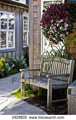 Stock Image - A wood bench and hanging flower basket along a path outside retail shops; Cannon Beach, Oregon, United States of America. Fotosearch