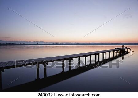 Stock Image - A wooden dock leading out to a tranquil lake at sunset; Starnberger See, Bavaria, Germany. Fotosearch