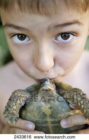 Stock Photograph - A young boy holding a kissing a small turtle; France. Fotosearch