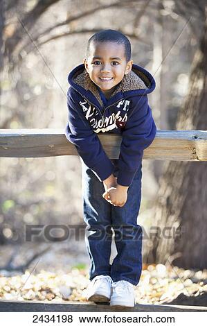 Stock Photo - A young boy leaning over a wooden fence smiling; San Francisco, California, United States of America. Fotosearch