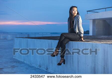 Stock Photo - A young female model posing on a roof at sunset; Xiamen, China. Fotosearch