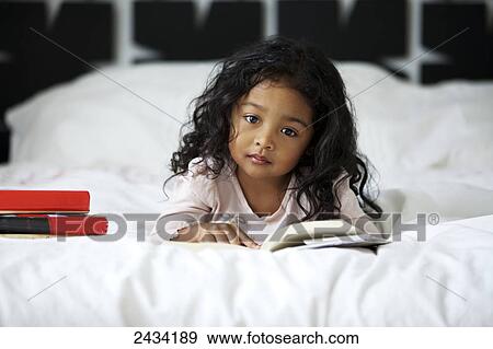 Stock Photo - A young girl laying on a bed reading books; San Francisco, California, United States of America. Fotosearch