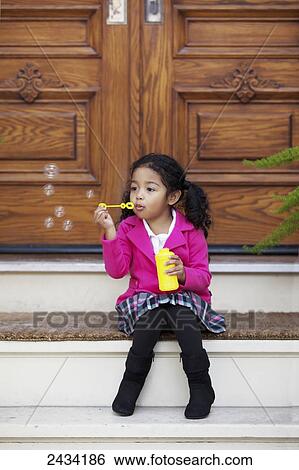 Stock Photograph - A young girl sits on steps blowing bubbles; San Francisco, California, United States of America. Fotosearch