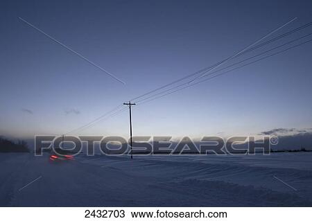 Stock Image - Car travelling along Old School Road at dusk in winter; Caledon, Ontario, Canada. Fotosearch