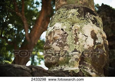 Stock Photo - Carved faces peer out from a temple in the Angkor Wat temple complex; Siem Reap, Cambodia. Fotosearch