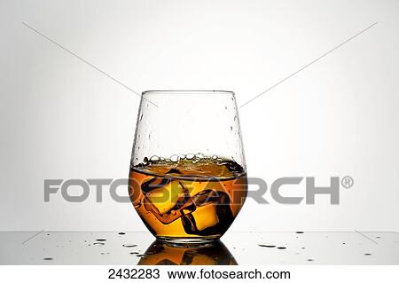Stock Image - Close up ice cubes being dropped into a glass of whiskey and splashing; Calgary, Alberta, Canada. Fotosearch