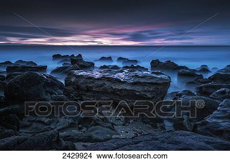 Picture - Clouds glowing at sunset over the ocean from the rocky coast; Tarifa, Cadiz, Andalusia, Spain. Fotosearch