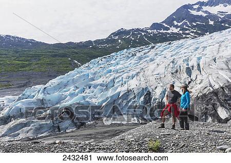 Stock Image - Couple standing on overlook in front of Shoup glacier, Shoup Bay State Marine Park, Prince William Sound; Valdez, Alaska, United States of America. Fotosearch