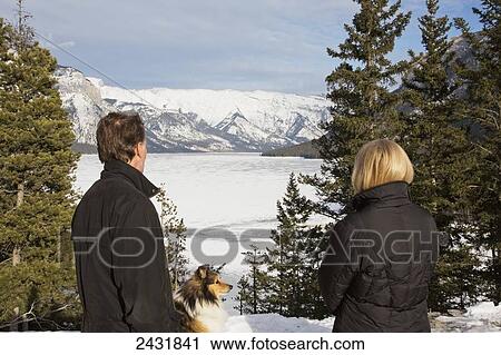 Stock Image - Couple with a dog looking from viewpoint at Lake Minnewanka; Banff, Alberta, Canada. Fotosearch