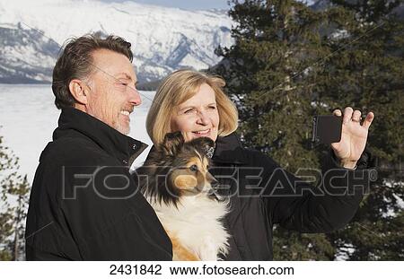 Stock Image - Couple with a dog taking a selfie from viewpoint on Lake Minnewanka; Banff, Alberta, Canada. Fotosearch
