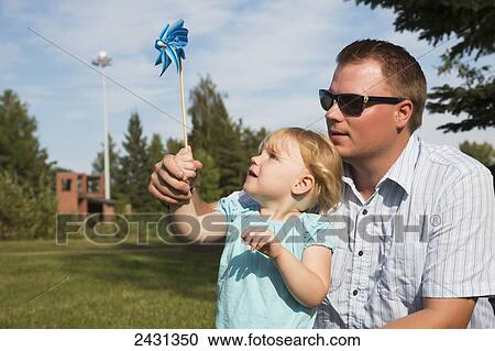 Stock Image - Father and daughter with a pinwheel in a park; Edmonton, Alberta, Canada. Fotosearch