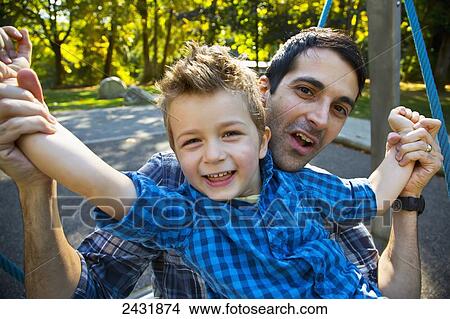 Picture - Father and son having fun together at a playground on a dish swing; Langley, British Columbia, Canada. Fotosearch